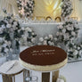 Decorative cake with 'Just Married' inscription on a table with floral arrangements and a chandelier in the background.